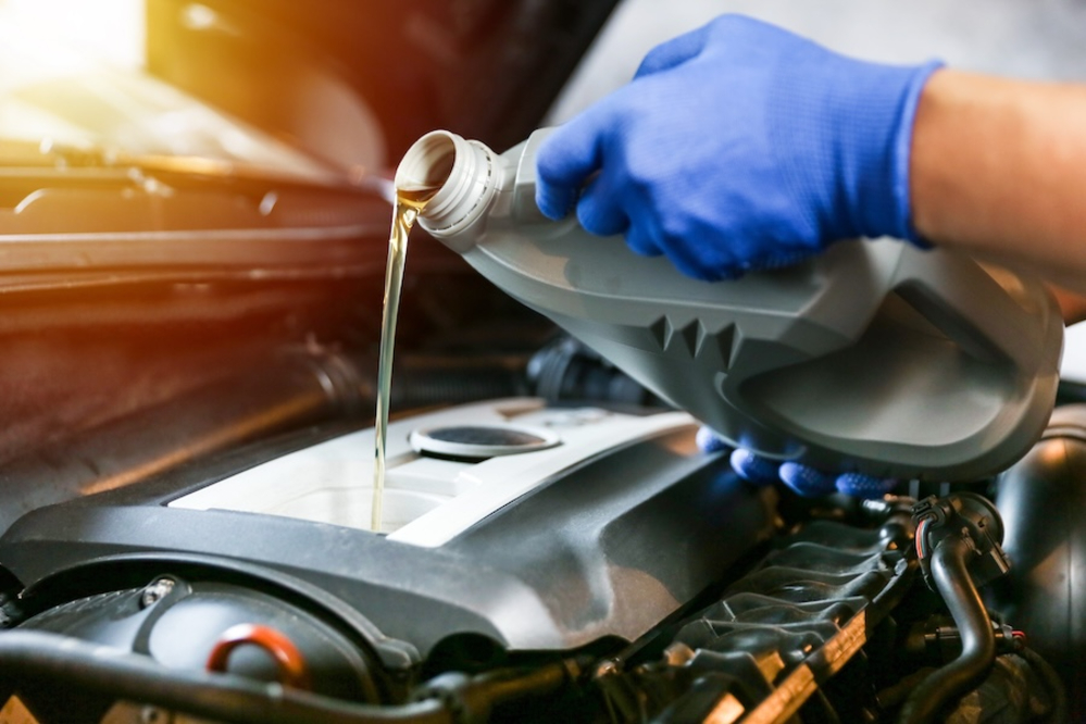A technician in blue gloves pouring motor oil into a car’s engine
