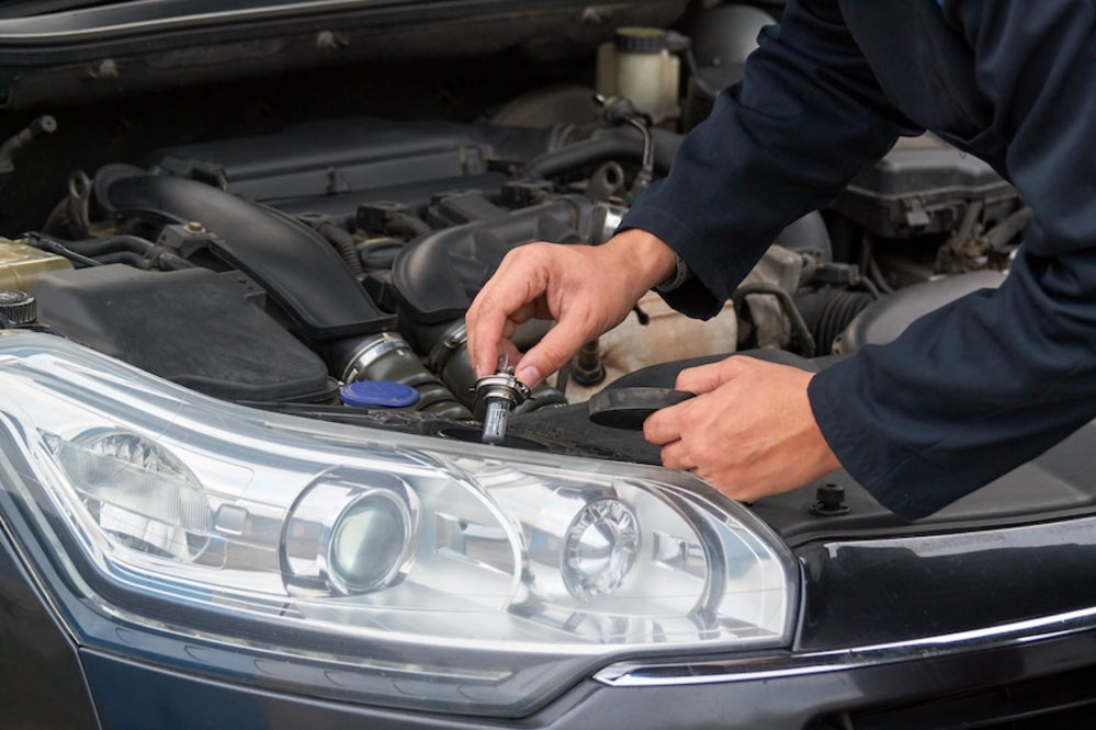 A mechanic replacing the bulb in a vehicle’s headlight 