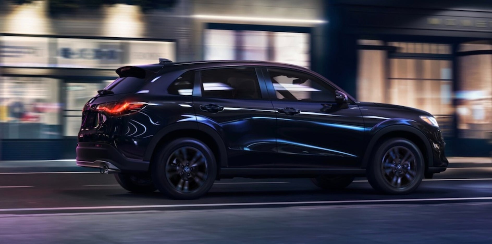 A black 2026 Honda HR-V SUV driving down a city street at night
