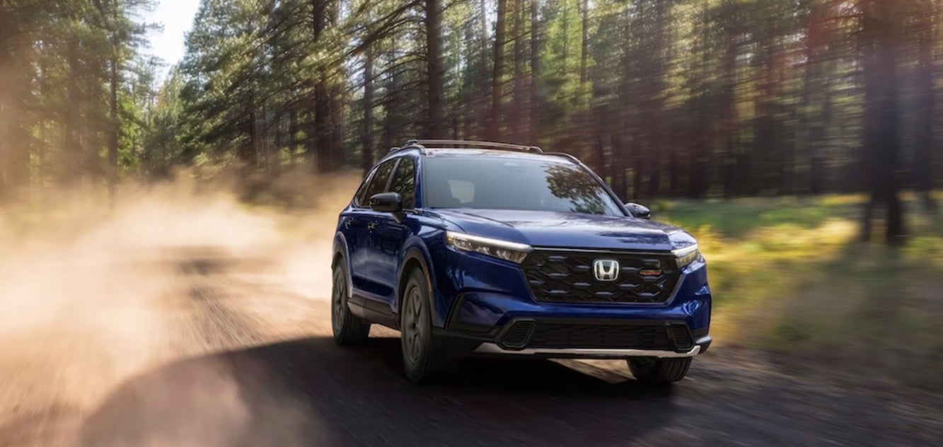A blue 2026 Honda CR-V SUV driving down a dusty wooded road