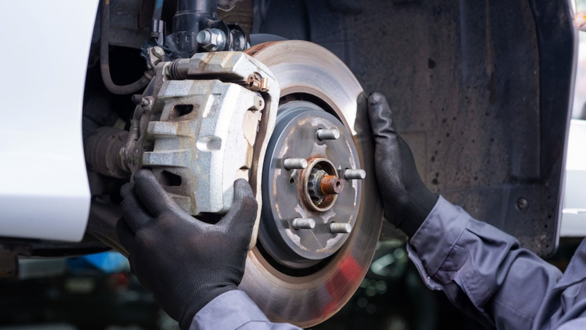 A person wearing blue coveralls and black gloves working on the brakes of a vehicle