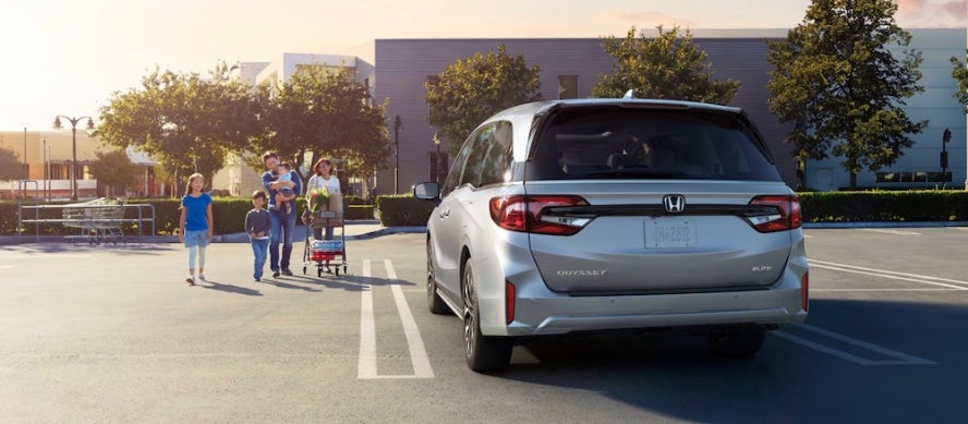 A family walking toward a silver 2026 Honda Odyssey minivan parked at a shopping center
