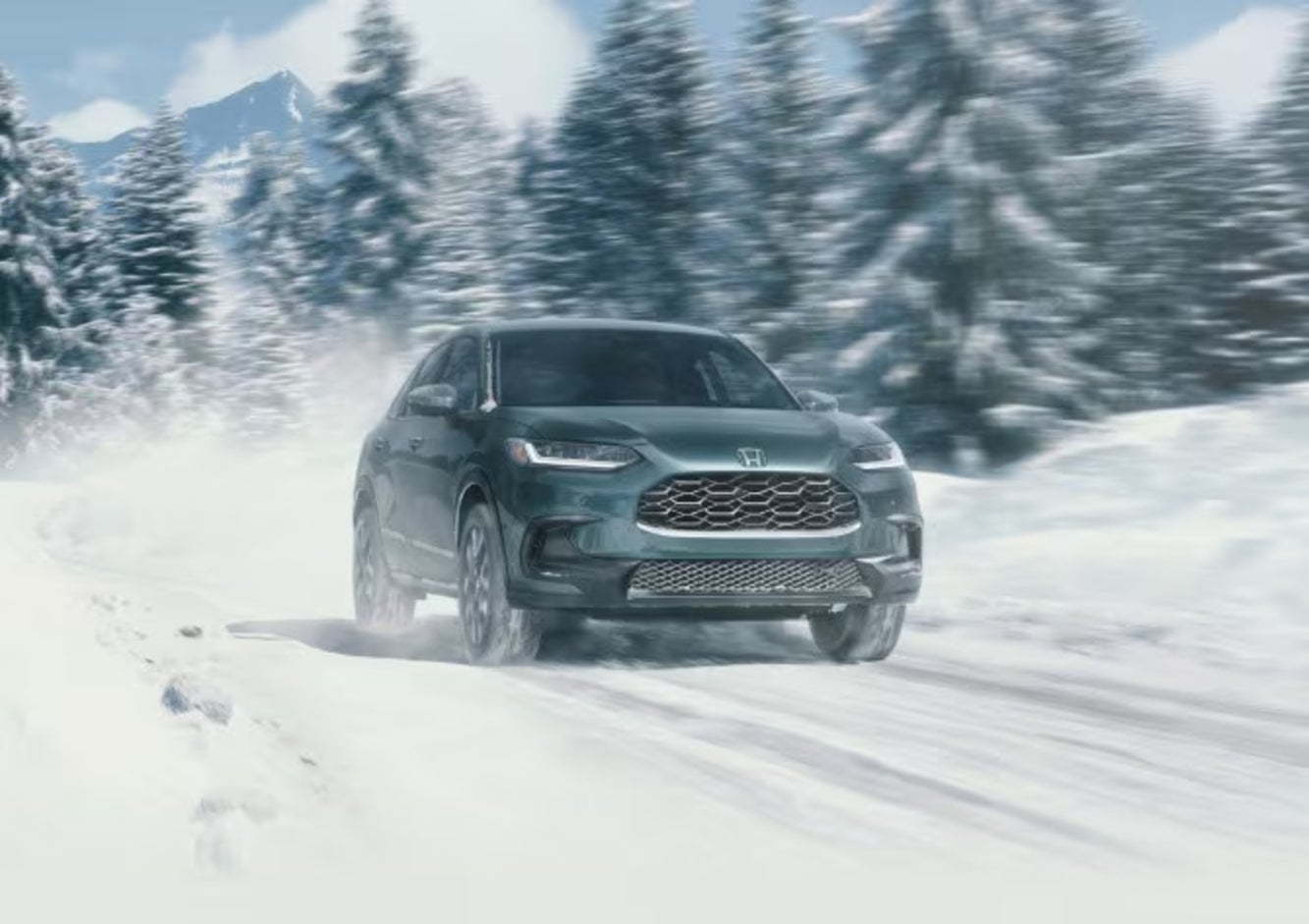 A green 2026 Honda HR-V SUV driving down a snow-covered road, with pine trees in the background
