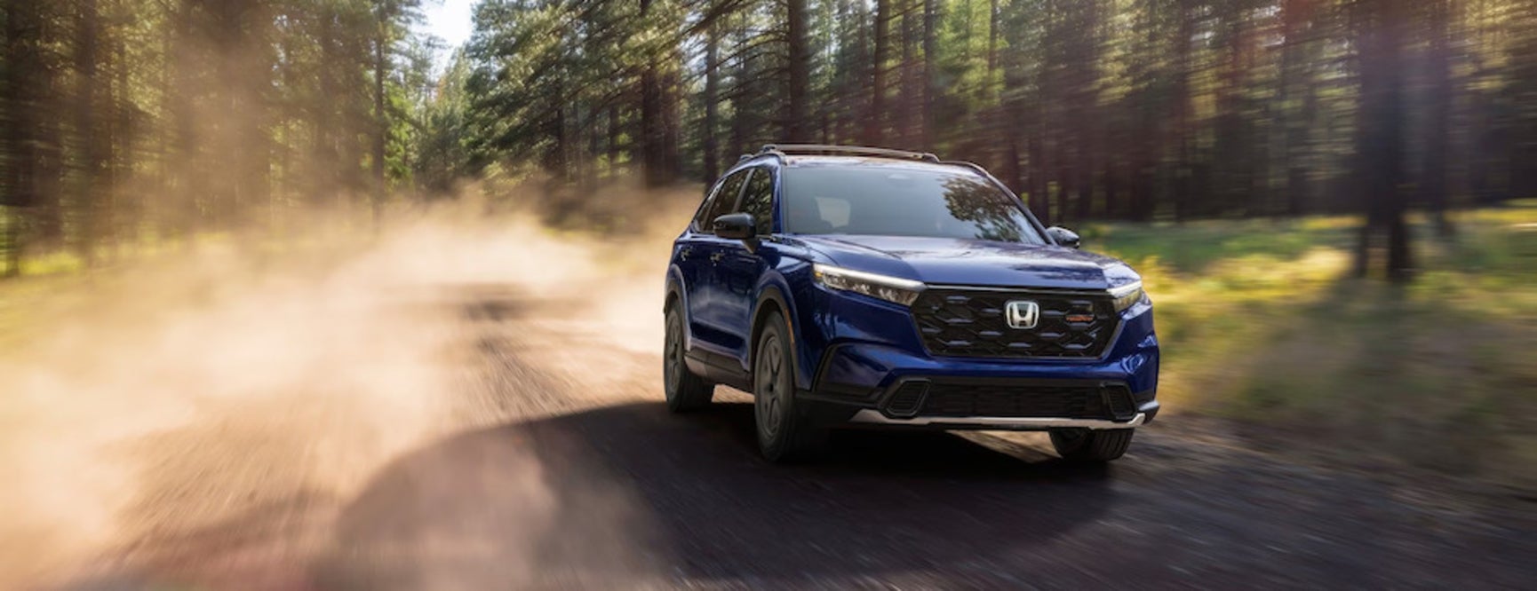 A blue 2025 Honda CR-V driving down a wooded dirt road