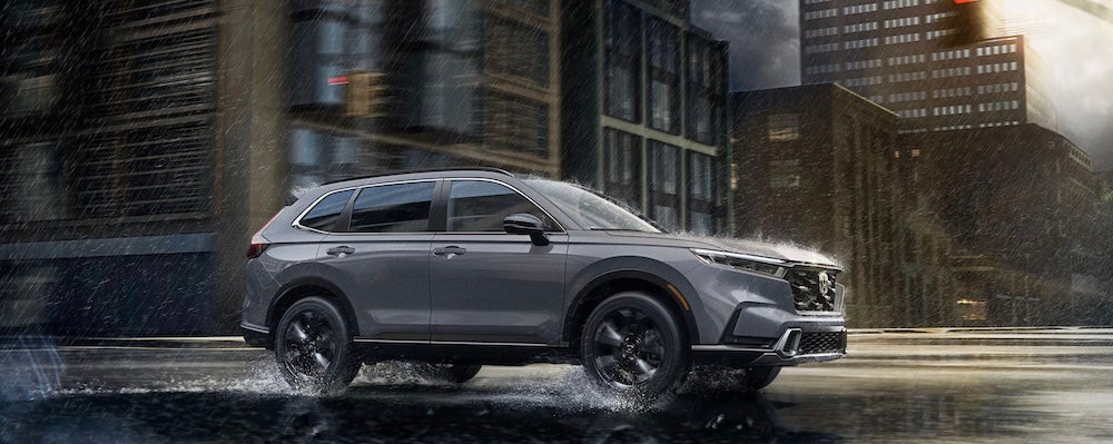 A gray 2026 Honda CR-V Hybrid SUV driving through a city in the rain
