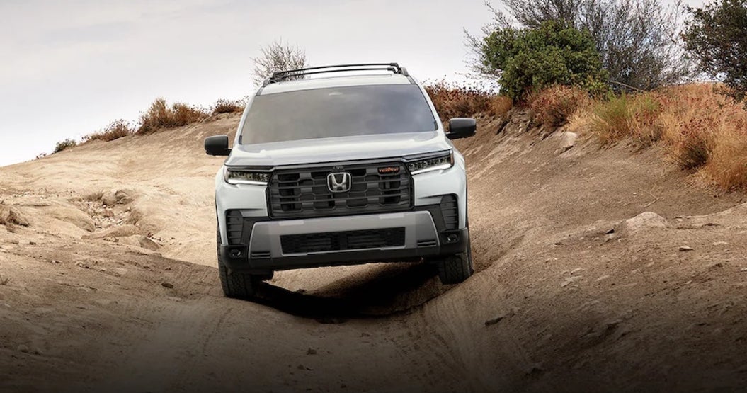 A white 2026 Honda Pilot SUV driving down a dirt trail