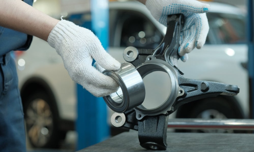 A person wearing white gloves repairing a vehicle’s front suspension