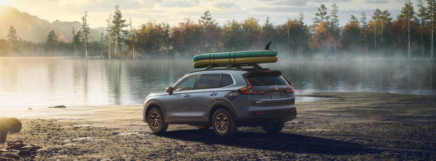 A gray Honda CR-V SUV with a roof rack parked at the edge of a lake