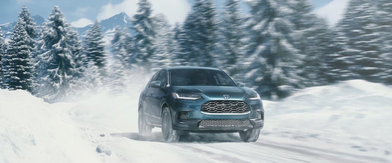 A front view of a light green 2025 Honda HR-V SUV driving through a snowy forest